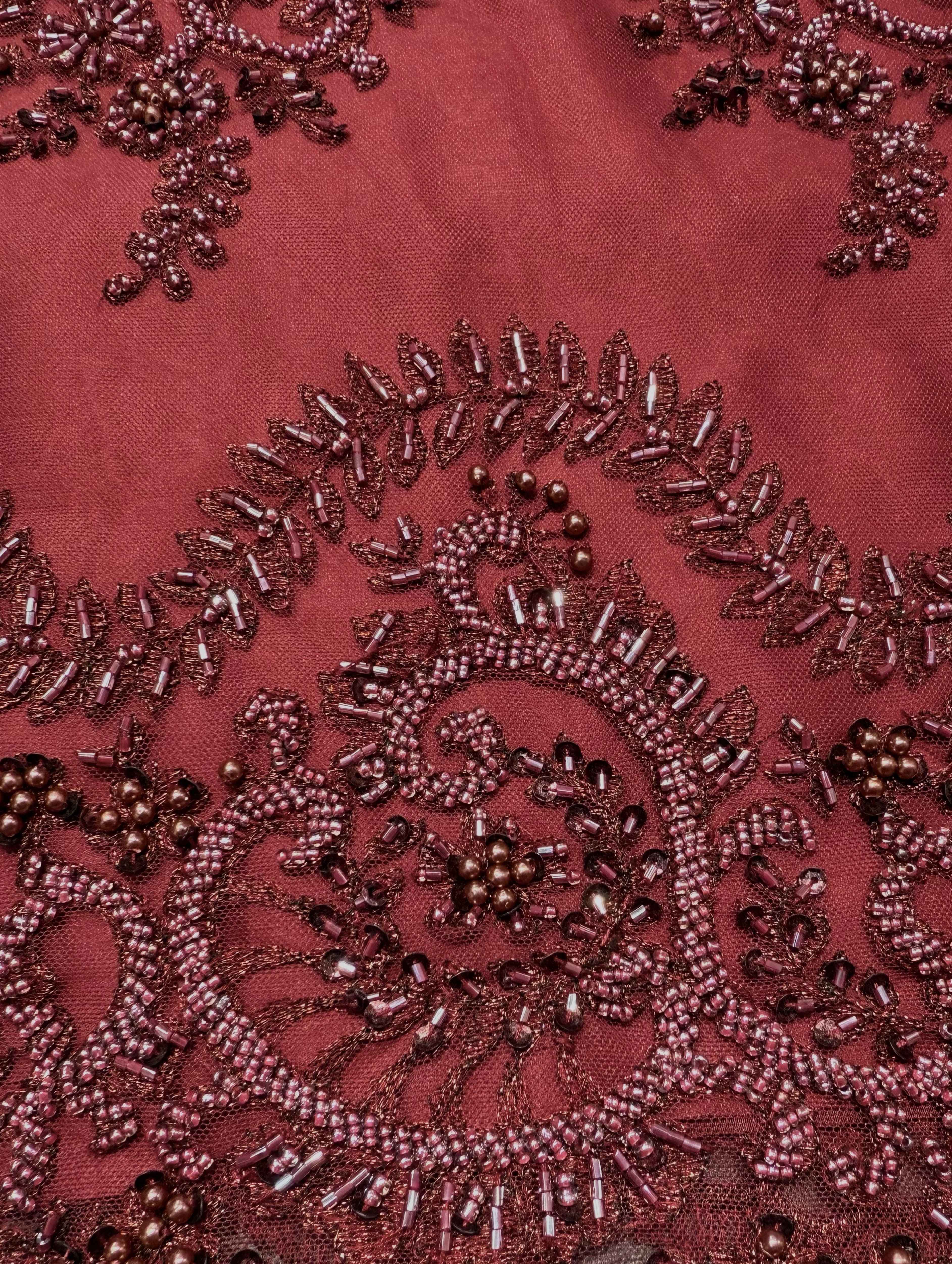 Detailfoto van bordeaux kant stof met verfijnde parels en kralen, zichtbaar patroon en textuur, ideaal voor avondjurk en traditionele kleding