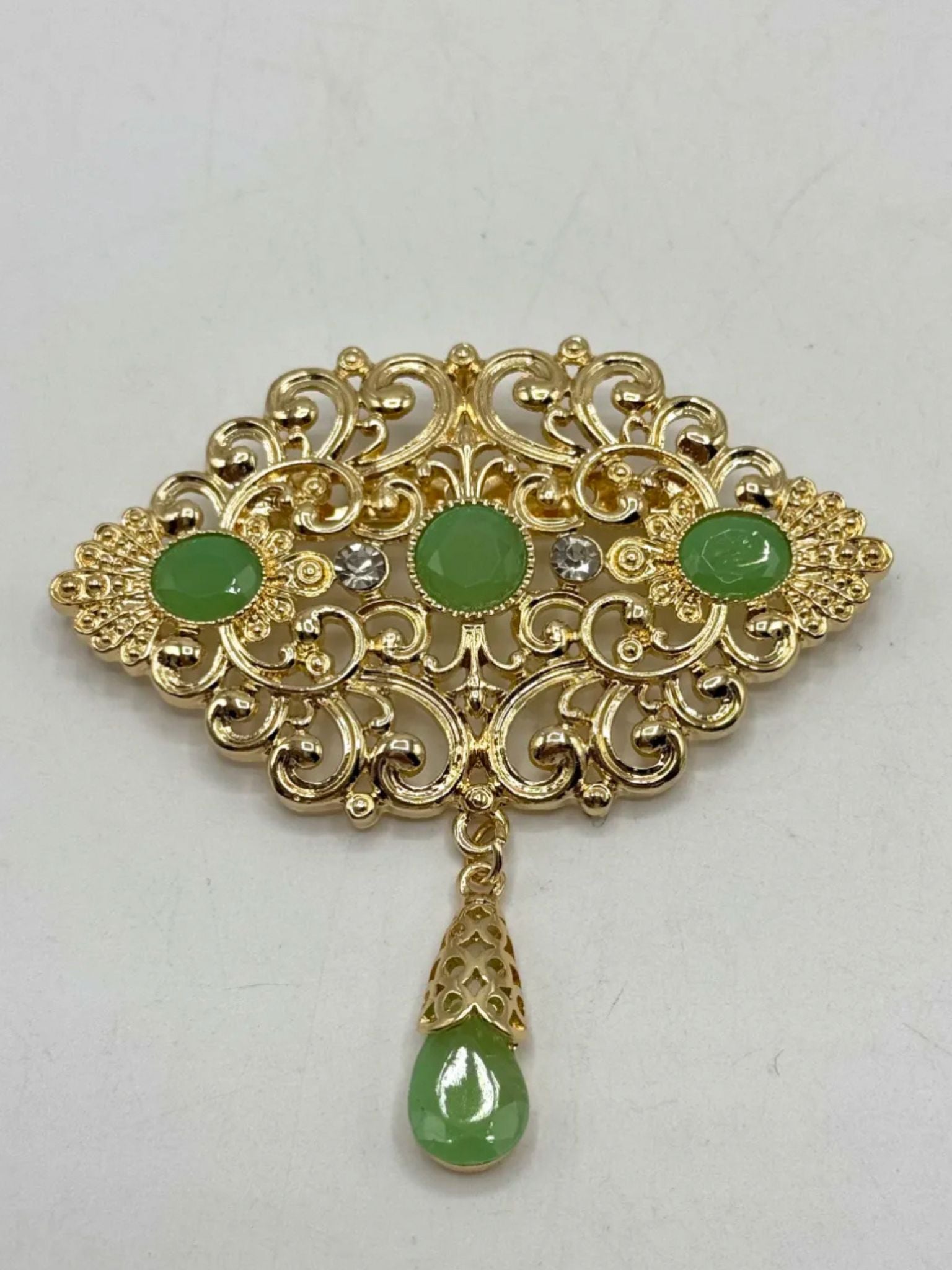 Elegante gouden broche met mintgroene stenen, perfect als accessoire bij takshita of feestelijke kleding.