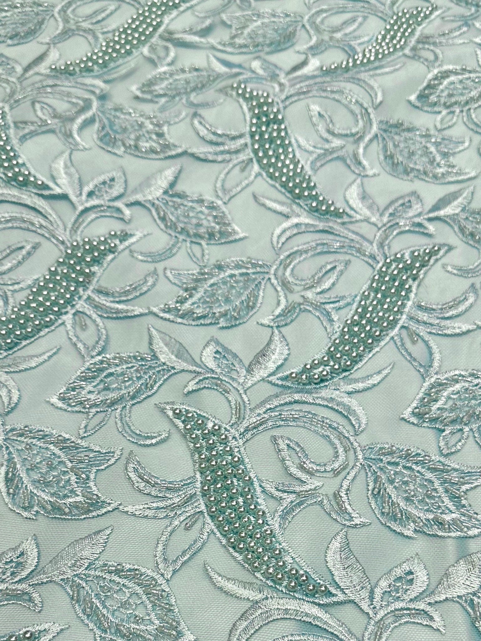 Detailfoto van blauwgroene kant stof met verfijnde parels, zichtbaar patroon en textuur, ideaal voor avondjurk en traditionele kleding