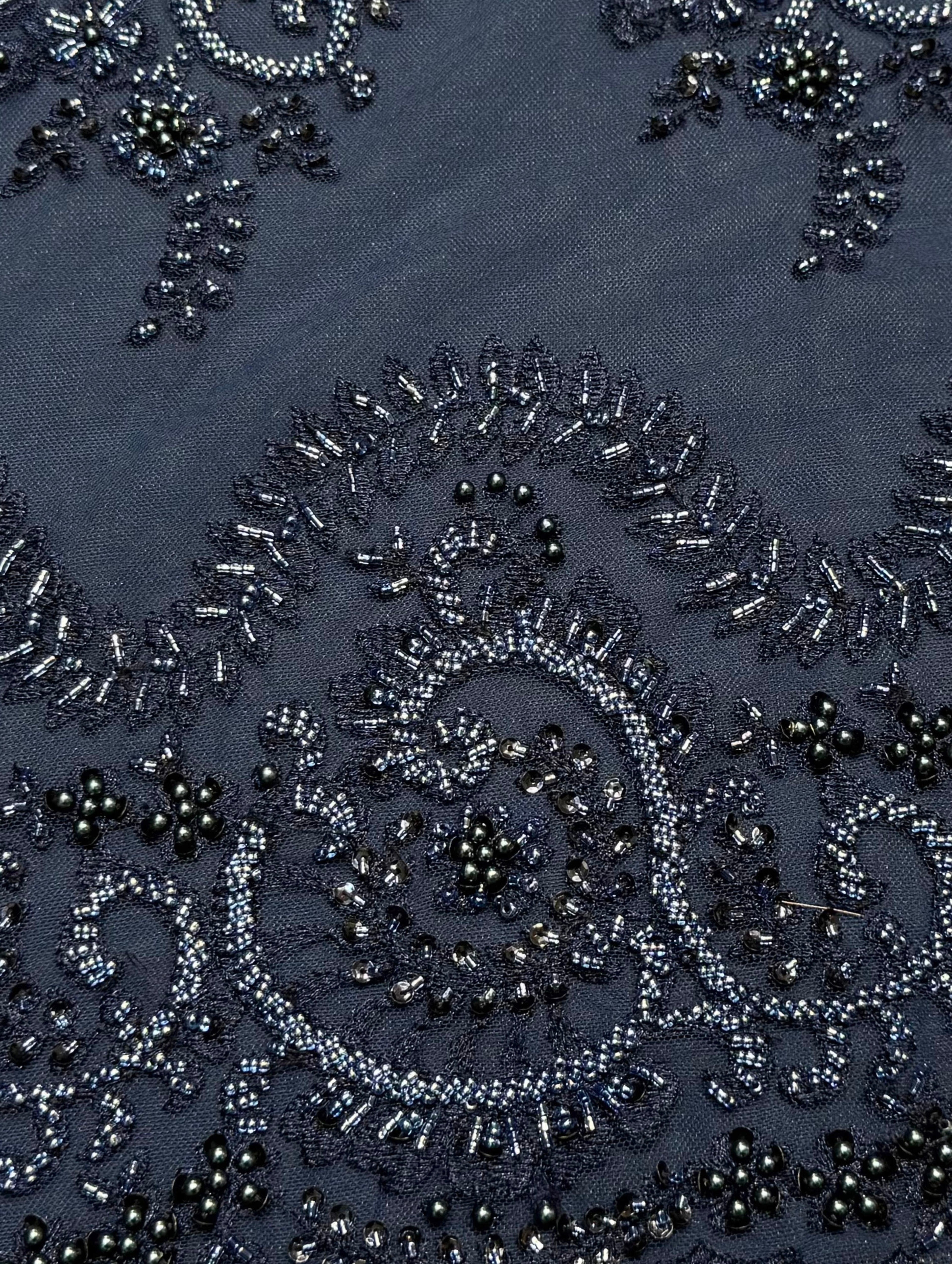 Detailfoto van donkerblauwe kant stof met verfijnde parels en kralen, zichtbaar patroon en textuur, ideaal voor avondjurk en traditionele kleding