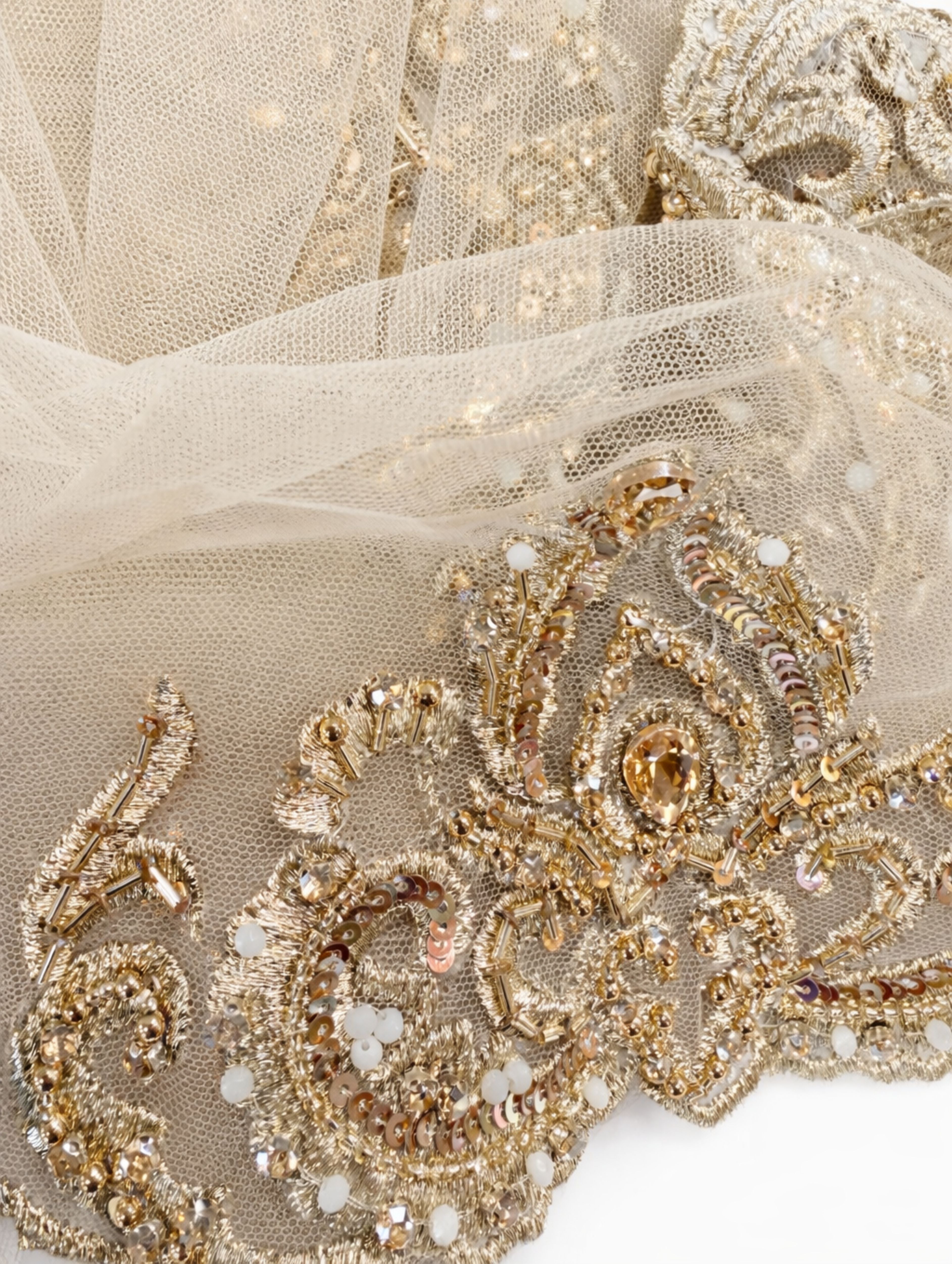 Detail van geborduurde rand van bruidssluier met gouden borduursel, parels en steentjes op beige tule.