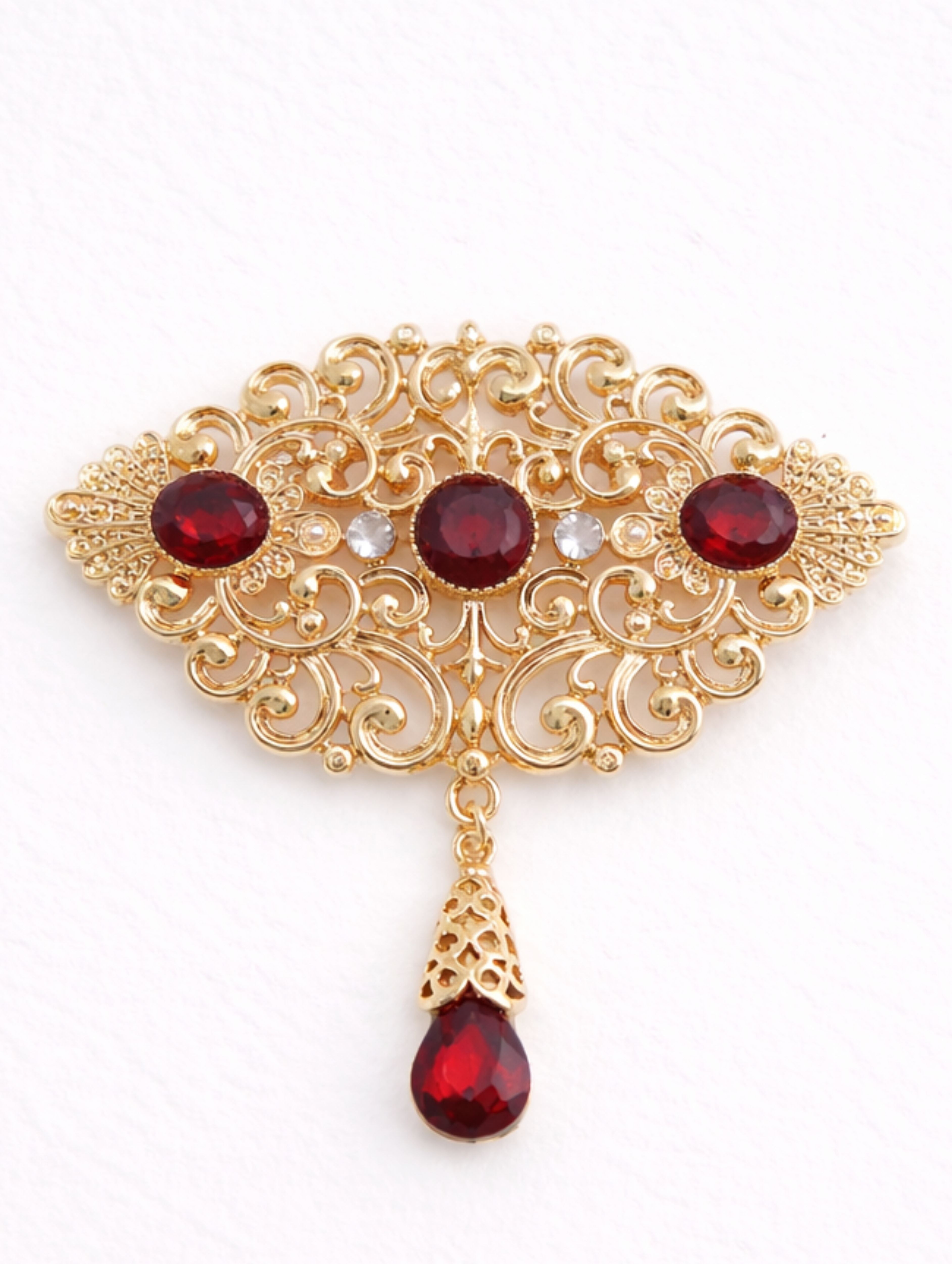 Gouden broche met rode stenen in goudkleurige afwerking, elegant vormgegeven en geschikt voor feestelijke en stijlvolle gelegenheden.
