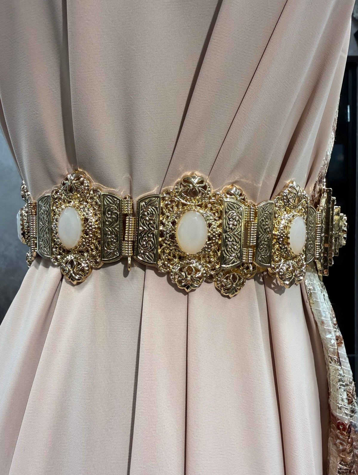 Gouden Marokkaanse Beldi mdamma riem met poederroze stenen, sierlijke metalen schakels en een decoratieve centrale sluiting.