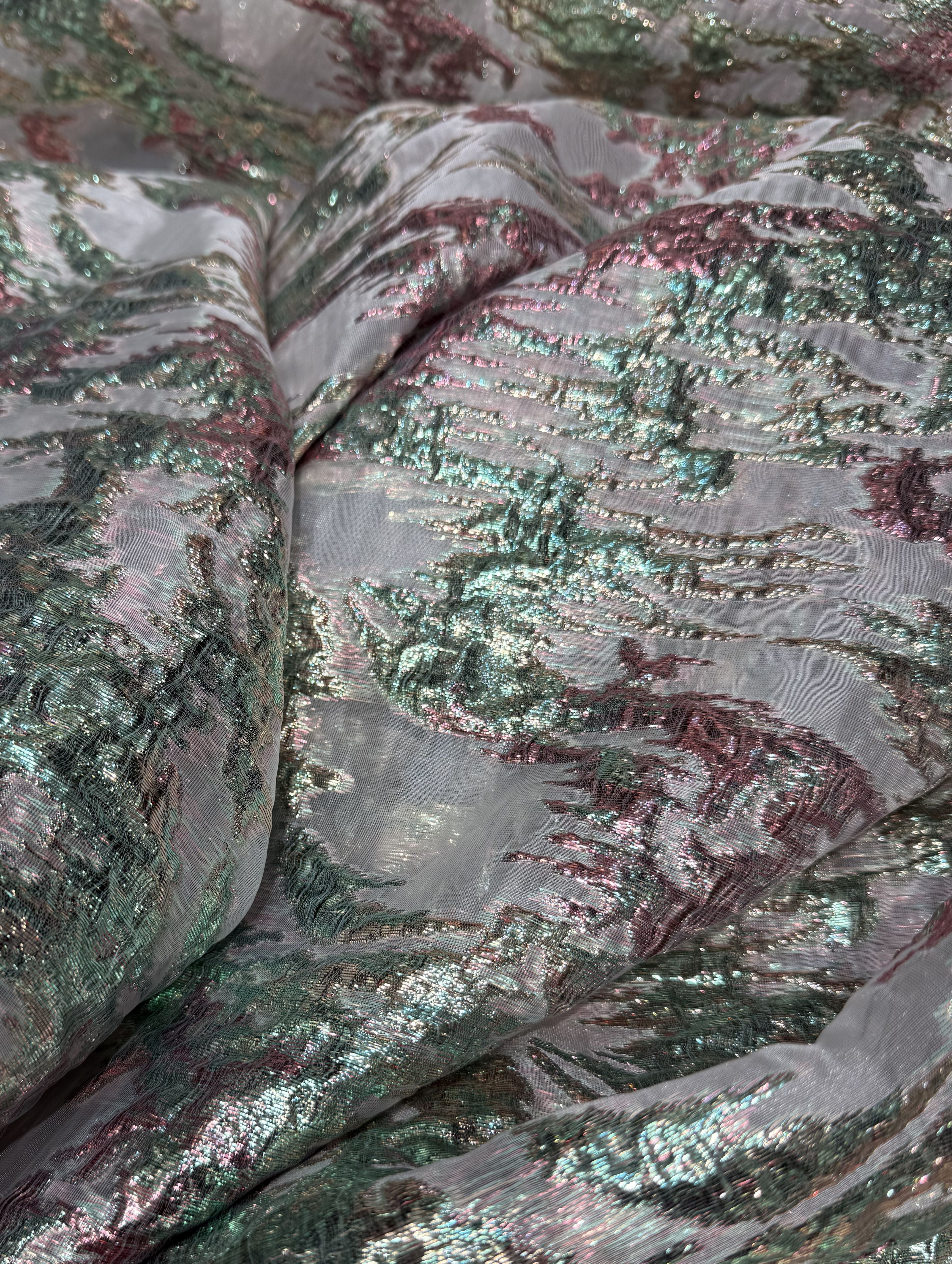 Luxe witte brokaat stof met glanzende groene en roze details op een transparante basis.