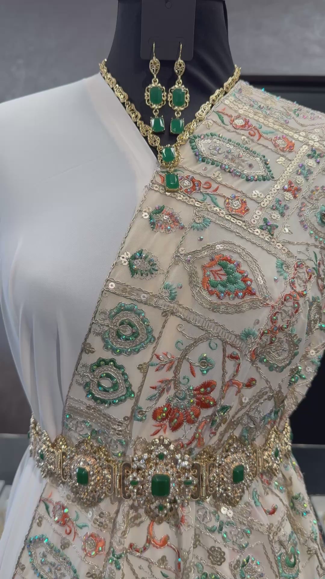 Video van crème sari stof met borduurwerk in groen en oranje tinten, waarbij de details en afwerking van de stof goed zichtbaar zijn. Ideaal voor elegante traditionele outfits.