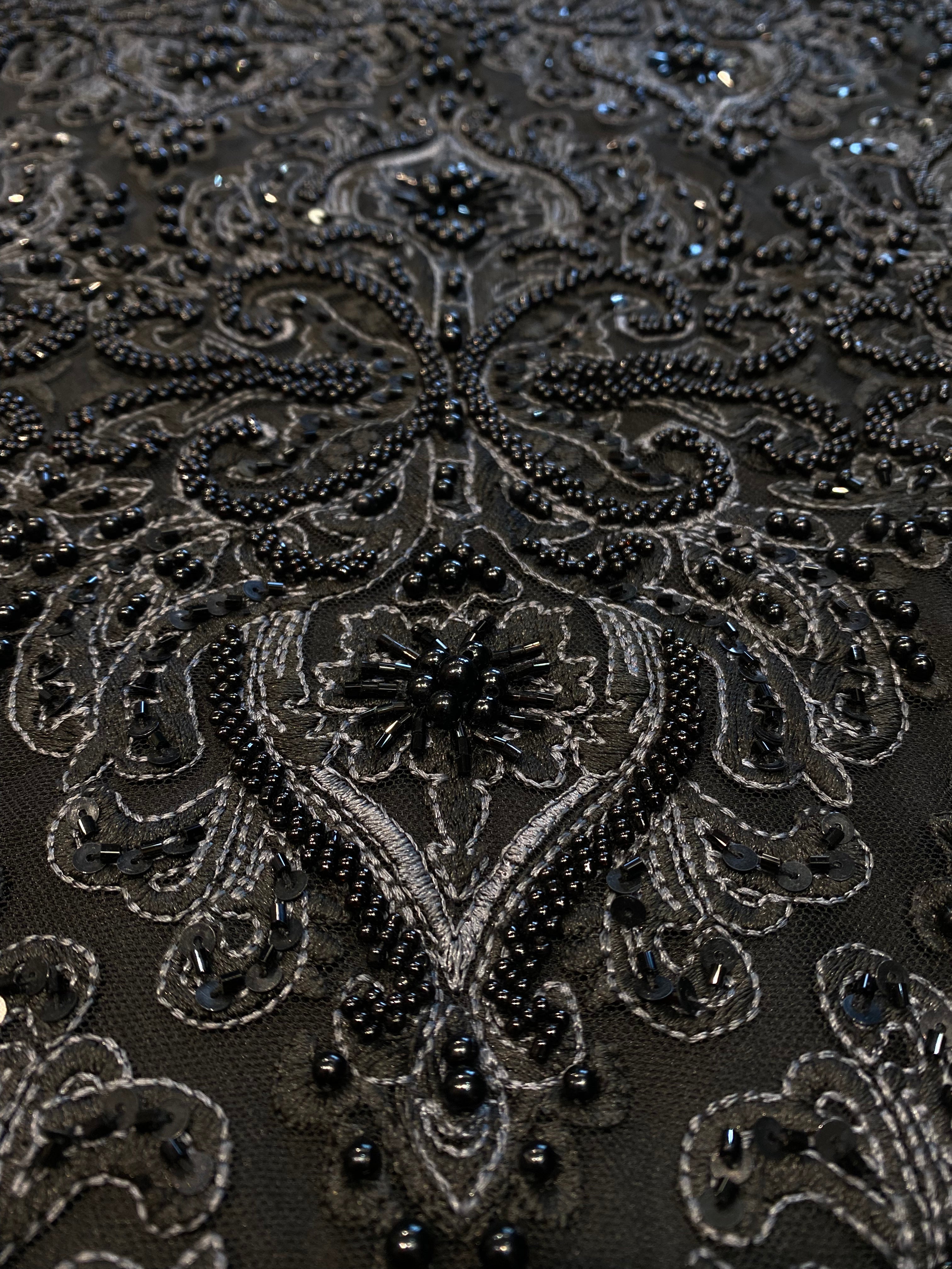 Detailfoto van zwarte kant stof met verfijnde parels en kralen, zichtbaar patroon en textuur, ideaal voor avondjurk en traditionele kleding